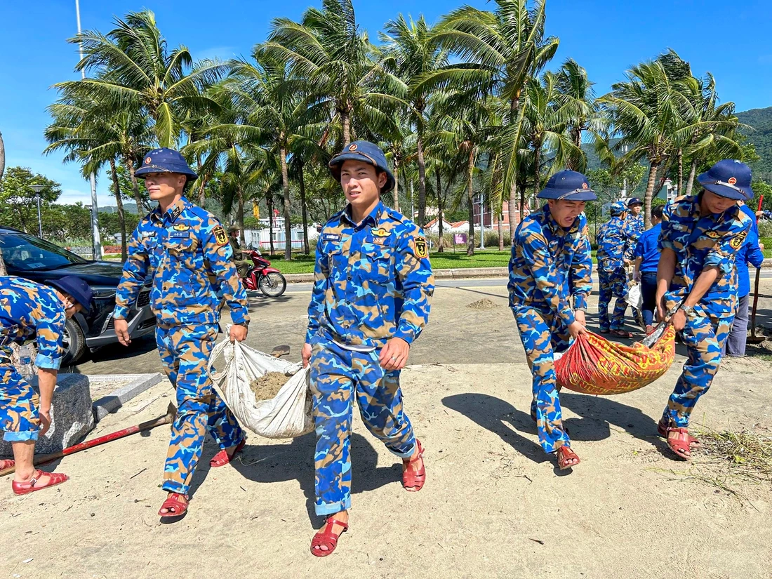 Các cán bộ, chiến sĩ Lữ đoàn 161, Bộ Tư lệnh Vùng 3 Hải quân cùng vận chuyển lượng lớn cát biển bị sóng đánh trên tuyến đường Hoàng Sa (Đà Nẵng) sau cơn bão số 13 tháng 11-2025 - Ảnh: THANH NGUYÊN
